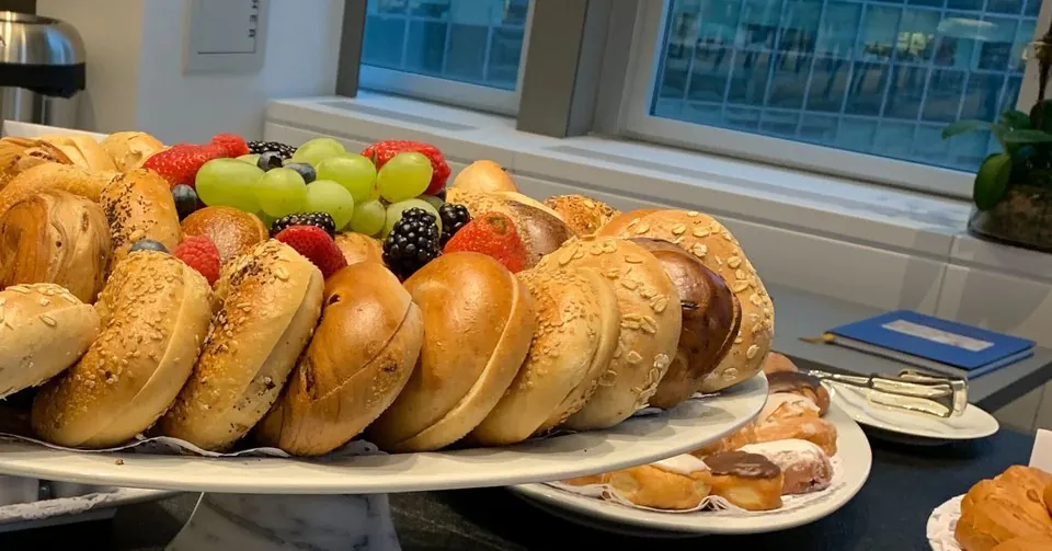 Bagel and fresh fruit platter on a marble stand beside pastries at a morning meeting
