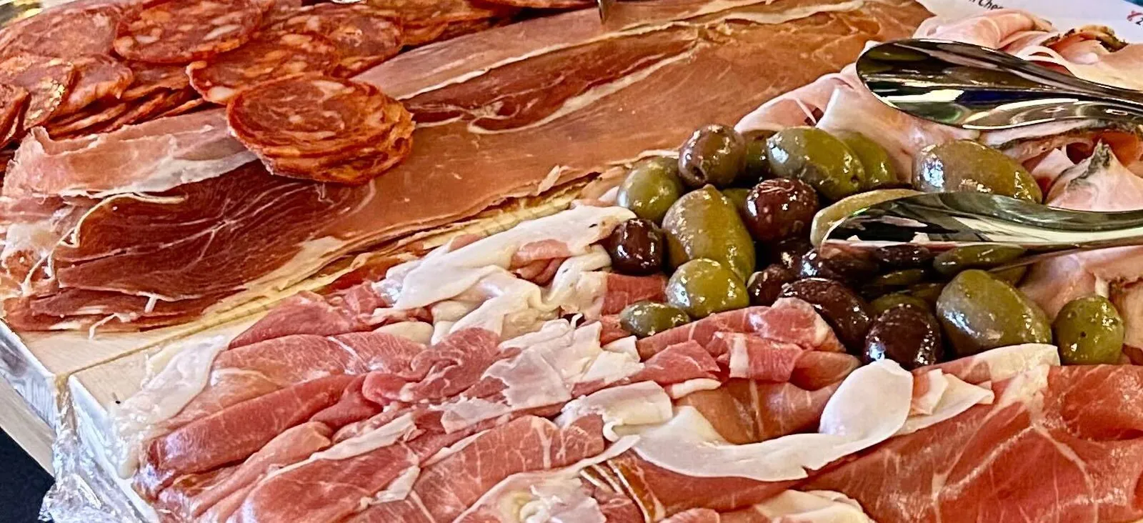 Cold charcuterie board of prosciutto, salami, cured ham and olives on a wooden board