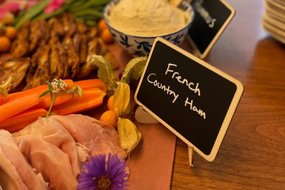 Cold catering table with sliced ham, hummus, carrots and a handwritten label on a wooden surface