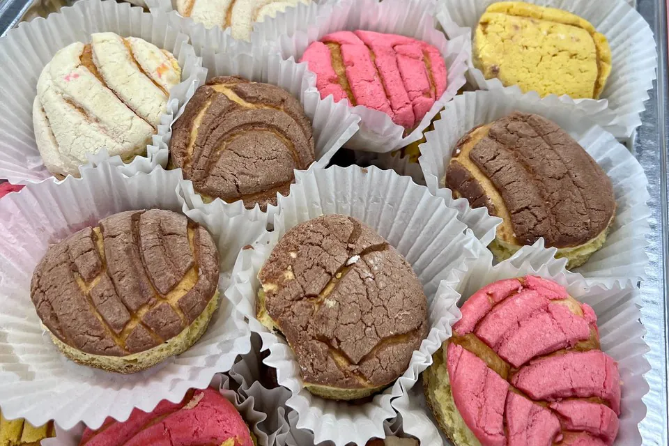 Foil tray of colorful conchas in individual paper liners ready for a break-room grab-and-go setup