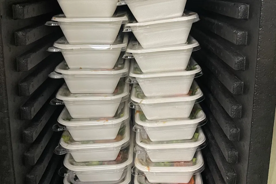 Two stacks of lidded individual meal containers held warm inside a black heating cabinet