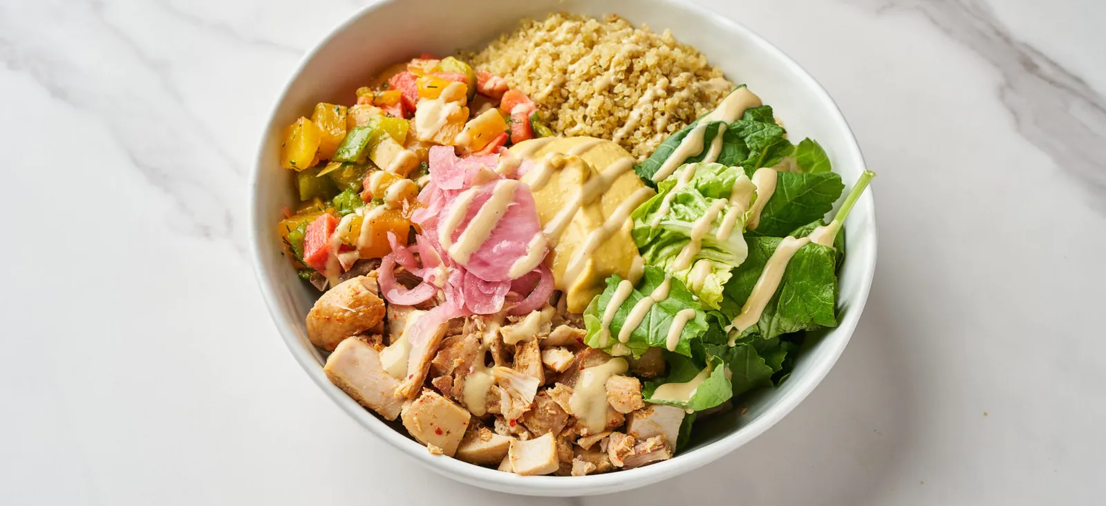 Overhead view of a Springbone Kitchen grain bowlwith quinoa, chicken, kale, roasted peppers and pickled onion on white marble