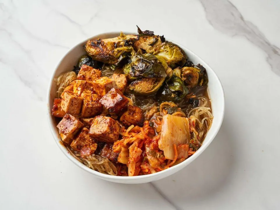 Springbone Kitchen noodle bowl with chili tofu,rice noodles, roasted brussels sprouts and kimchi in a white bowl