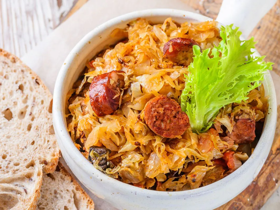 Bigos hunter's stew with kielbasa and sauerkrautin a stoneware crock beside slices of rye bread