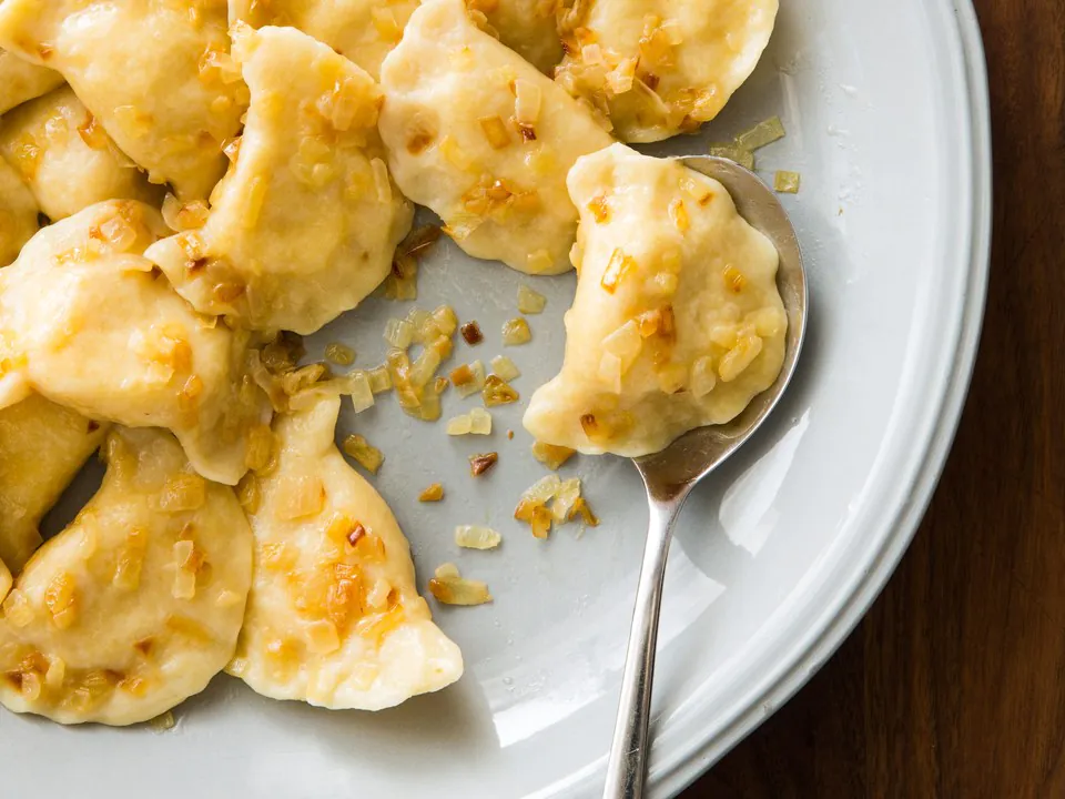 Ukrainian pierogi dumplings topped withcaramelised onions on a pale plate with a serving spoon