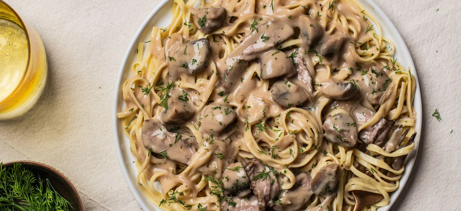 Beef stroganoff in mushroom cream sauce served overegg noodles on a white plate with fresh dill