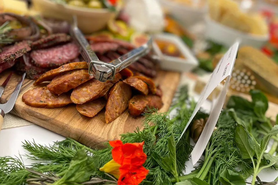 Close-up of a wooden board of sliced cured sausage and salami with serving tongs