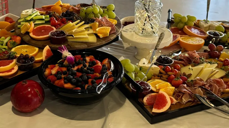Office table of separate catering trays holding cured meats, cubed cheese, fruit and dips