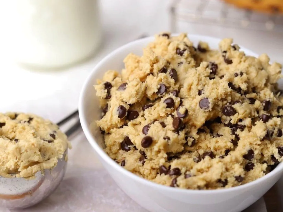 White bowl of chocolate chip edible cookie dough with a scoop beside it