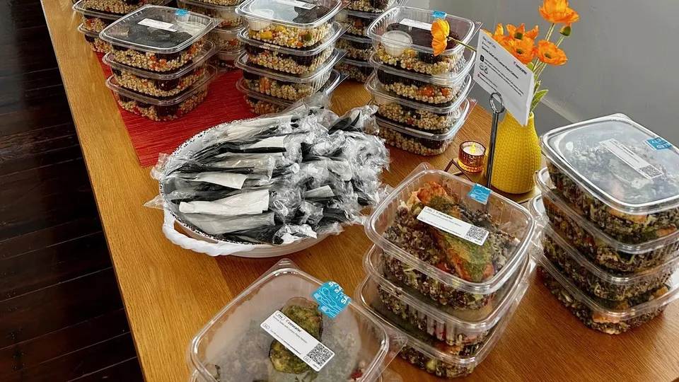 Rows of sealed single-serve containers stacked on a table beside a plate of individually wrapped cutlery