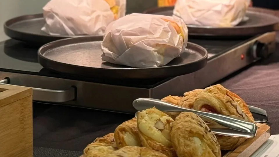Paper-wrapped breakfast sandwiches on dark plates beside a tray of almond pastries