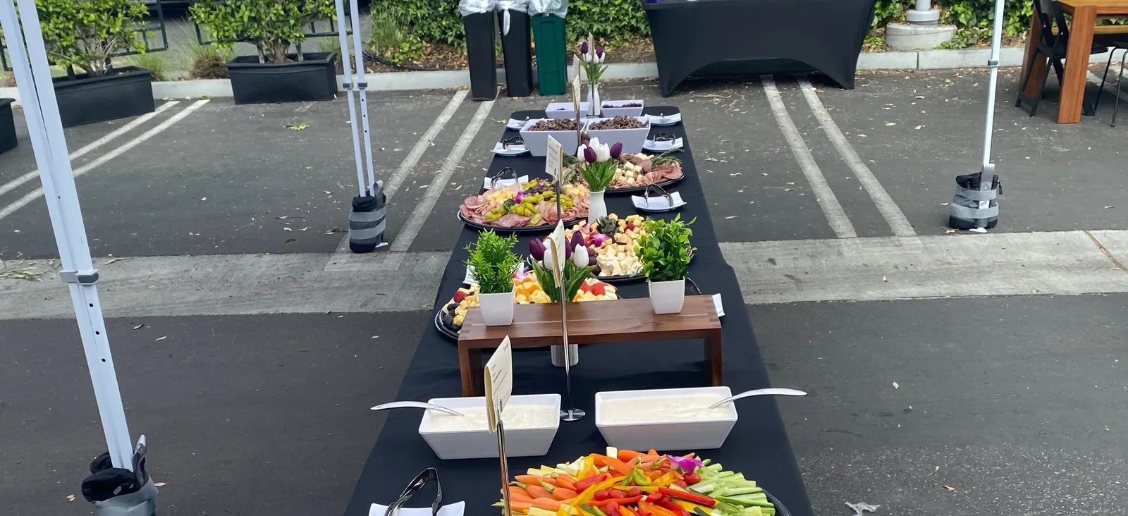 Long catered buffet table set up under white event tents in a parking lot on location
