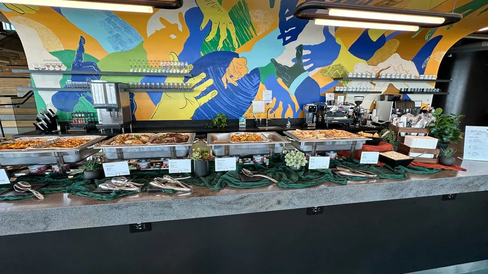 Long catering buffet line with chafing trays, serving spoons and stacked plates along a counter