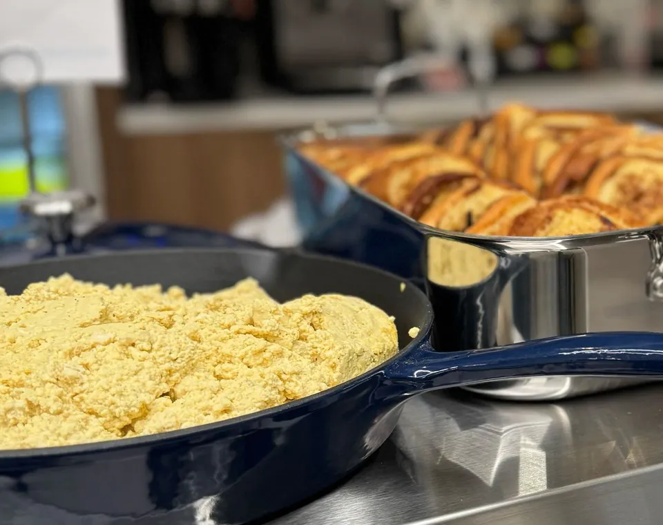 Scrambled eggs in a navy skillet beside a hotel pan of challah French toast on a stainless serving shelf in an office kitchen