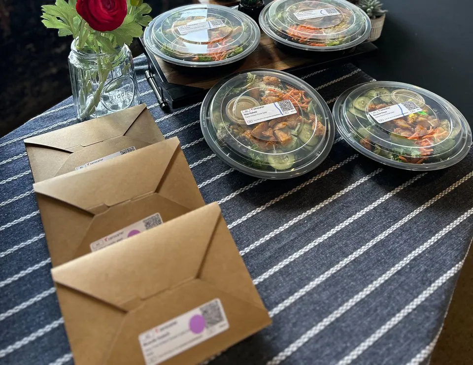 Individually packaged salad bowls and sealed kraft boxes with order labels laid out on a striped table runner in an office