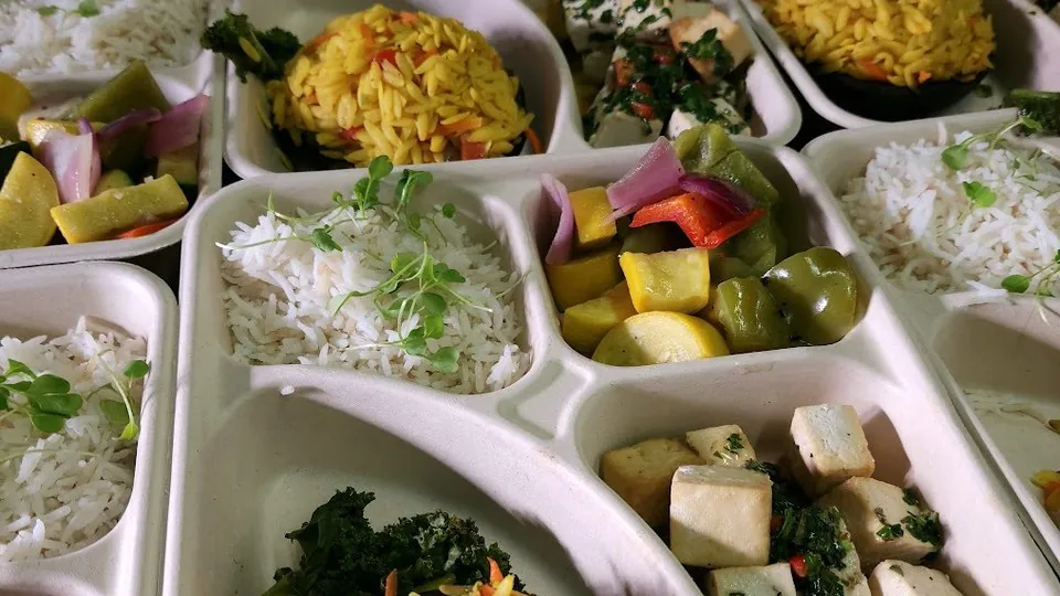 Rows of individual compartment trays with basmati rice, saffron orzo, marinated tofu and roasted squash prepared for a catering delivery