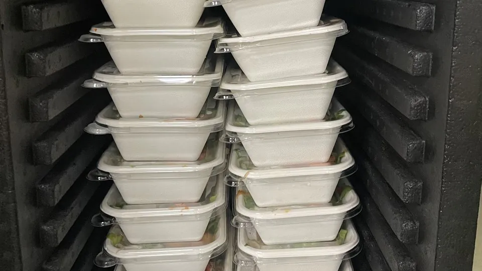 Two stacks of lidded individual meal containers inside a black insulated catering carrier