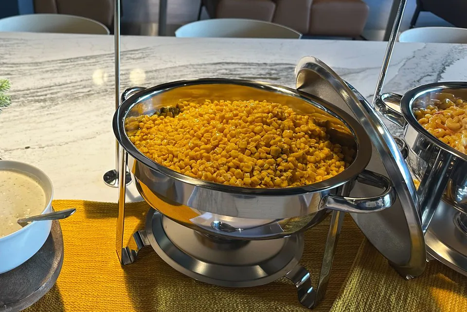 A stainless chafing dish on its stand with the lid open, holding a hot side dish on an office buffet table
