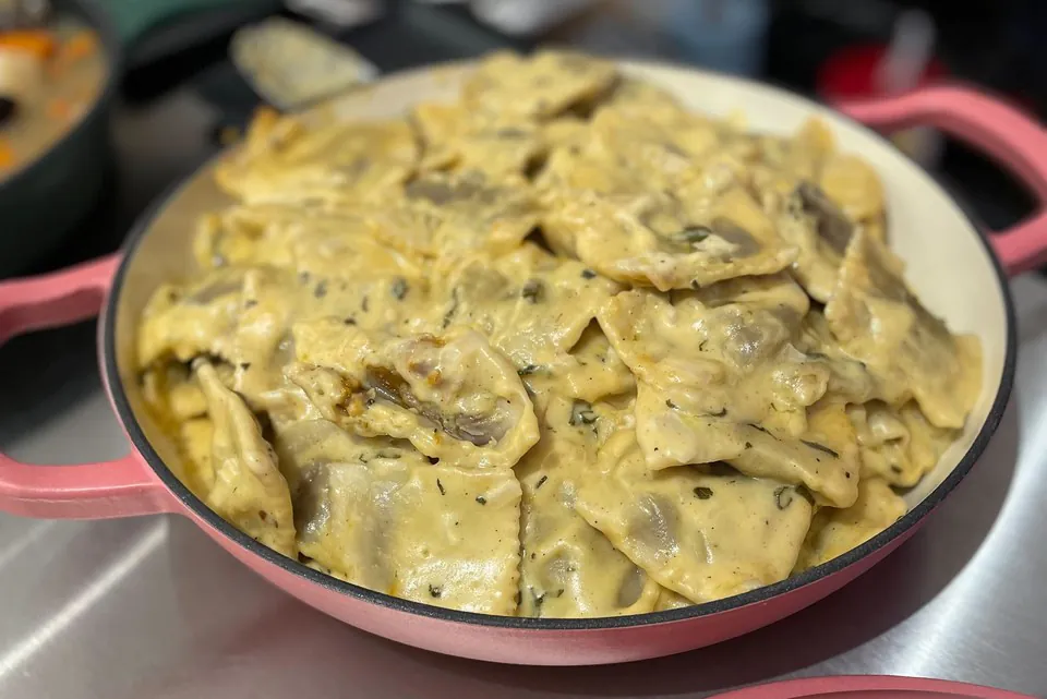 A single filled pan of creamy stuffed pasta with its lid resting beside it on a stainless counter