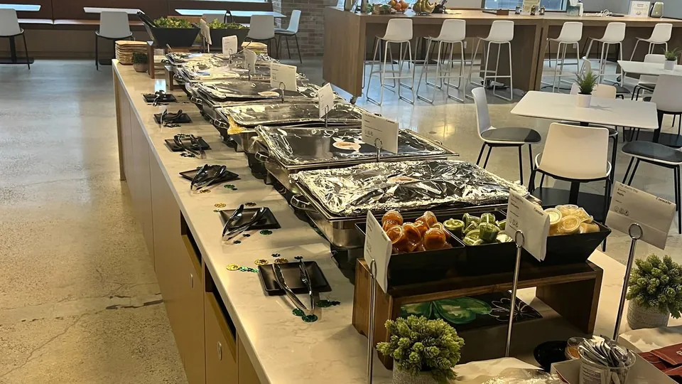 Office counter with a long row of foil chafing pans, a condiment caddy and a tray of plastic-wrapped cutlery at the near end