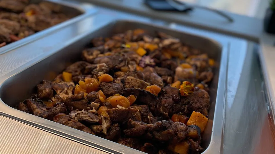 Stainless steel hotel pan of seasoned chicken and squash seated in a drop-in serving well beside a window