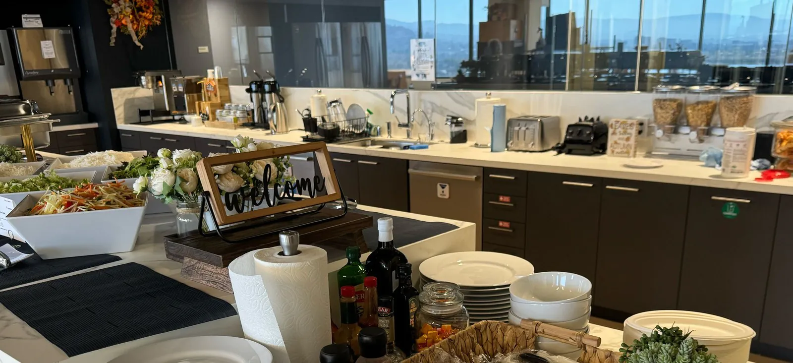 Office kitchen with a catered salad buffet on the left and the office's own coffee machines, toaster, cereal dispensers and snack jars along the right wall