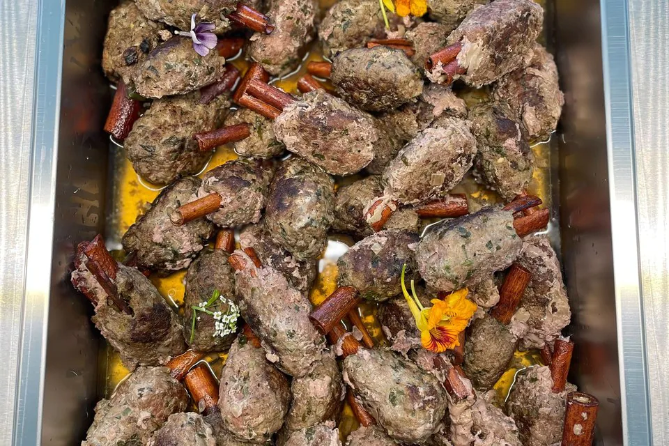 Grilled kofta in a catering pan Hotel pan of grilled Middle Eastern kofta with cinnamon and edible flowers at an office catering buffet