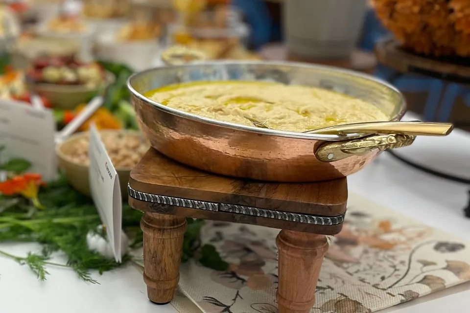 Hummus in a copper serving bowl Copper serving bowl of hummus finished with olive oil on a wooden riser at an office catering spread