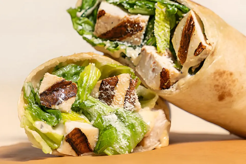 Two halves of a grilled chicken Caesar wrap, cut to show grilled chicken, romaine and Parmesan inside a flour tortilla