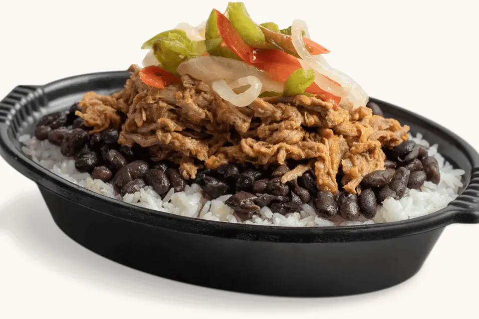 A black catering bowl of white rice and black beans topped with shredded mojo roast pork and a heap of sauteed onions and red and green peppers