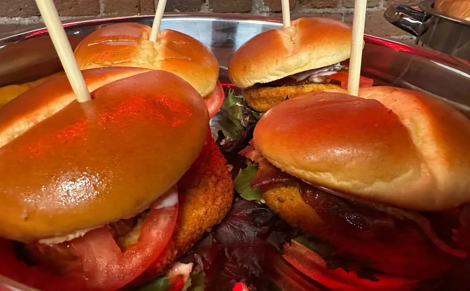 Close-up of sandwiches on soft toasted buns with wooden picks through them, sitting in a steel chafing pan