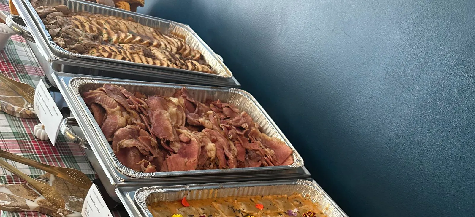 Chafing trays of carved turkey, maple glazed ham and sweet potato ravioli on a plaid tablecloth at an office Thanksgiving lunch