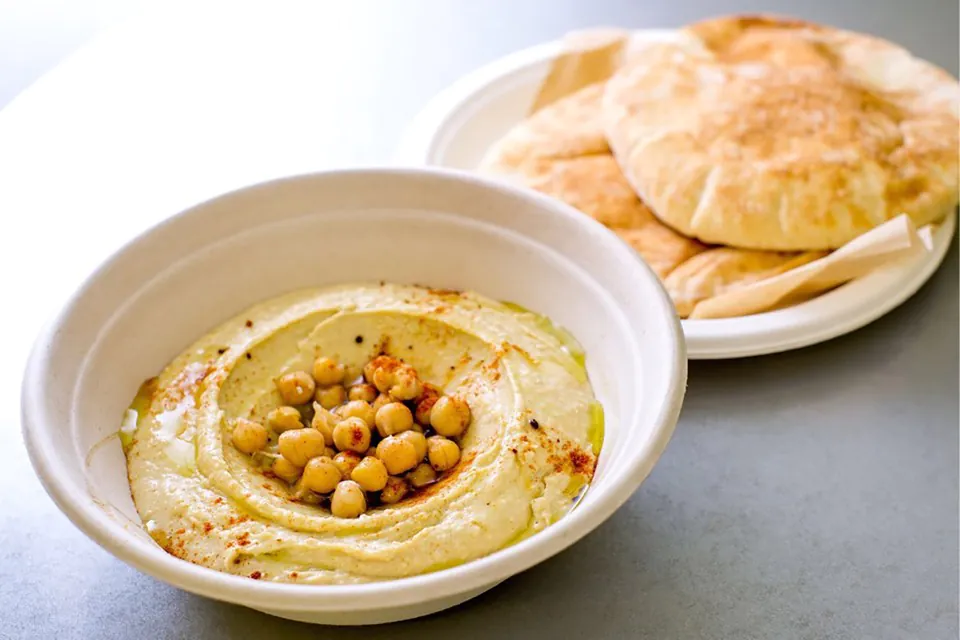 Hummus and pita from The Picnic Basket A bowl of hummus topped with whole chickpeas, paprika and olive oil, next to a plate of warm pita