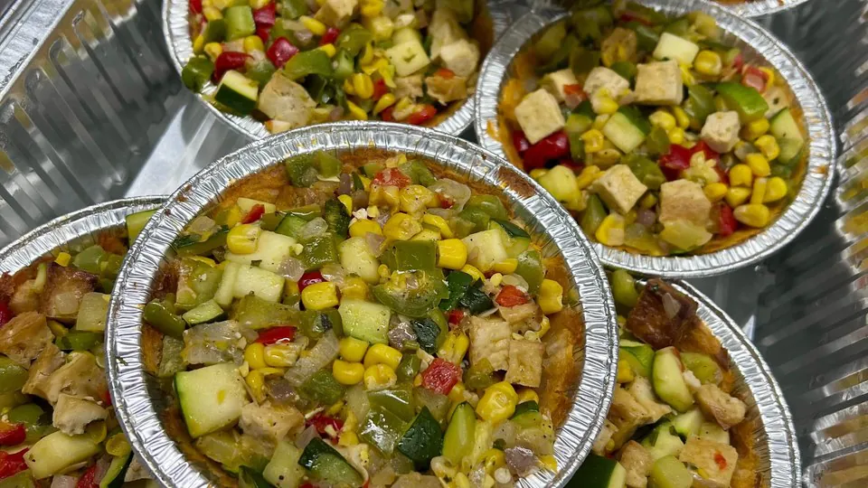 Individual foil serving bowls filled with corn, courgette, peppers and diced protein, packed side by side in a catering tray