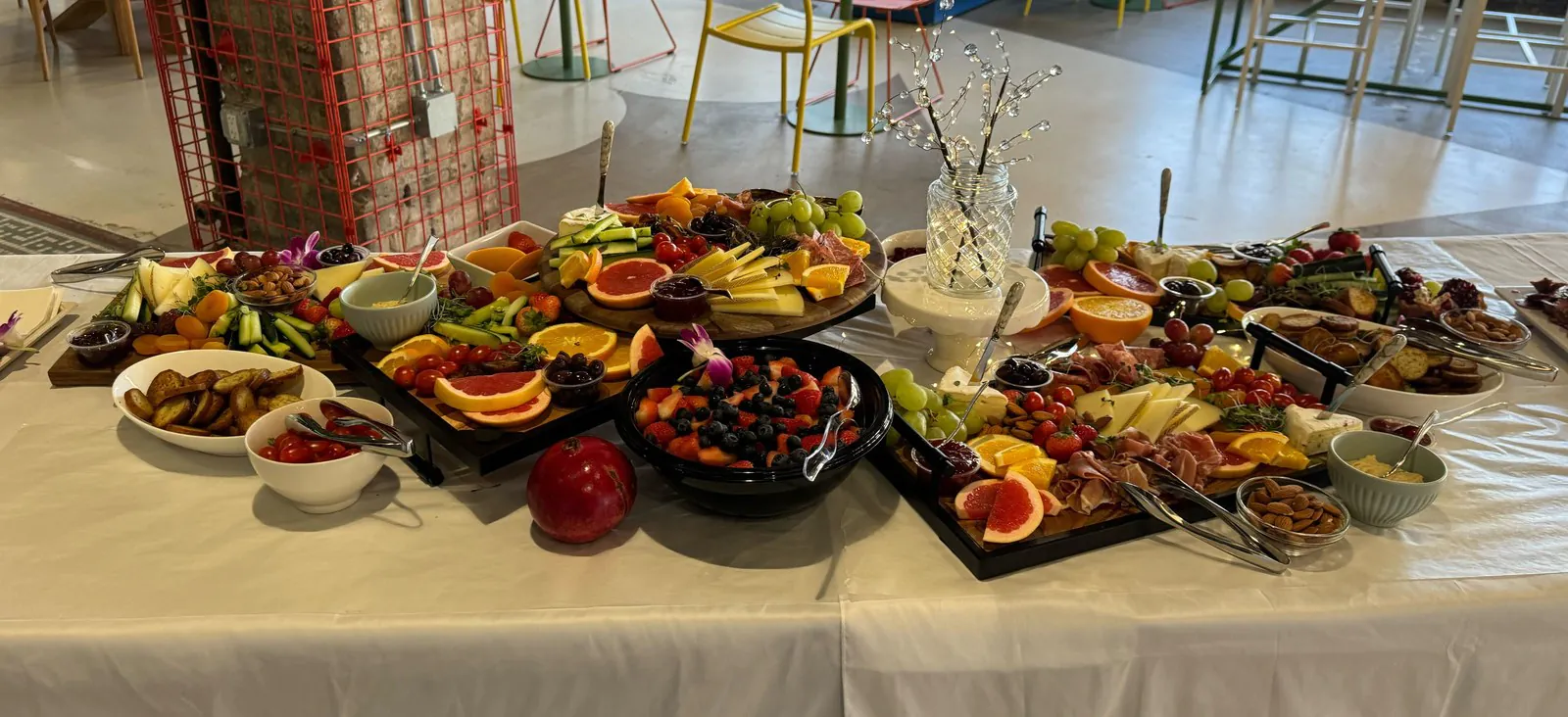 Long office table carrying six separate catering platters of cheese, cured meats, fruit and crudites