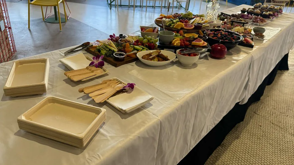 Stacked compostable trays and wooden forks waiting at the near end of a long catering table