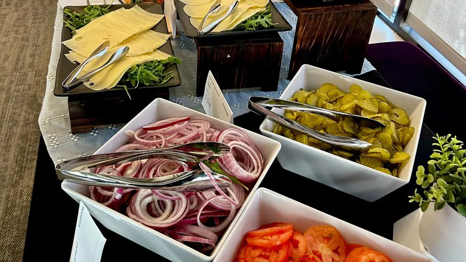 Build-your-own deli line with sliced cheeses, red onion, pickles and tomatoes each in a separate dish behind its own printed card