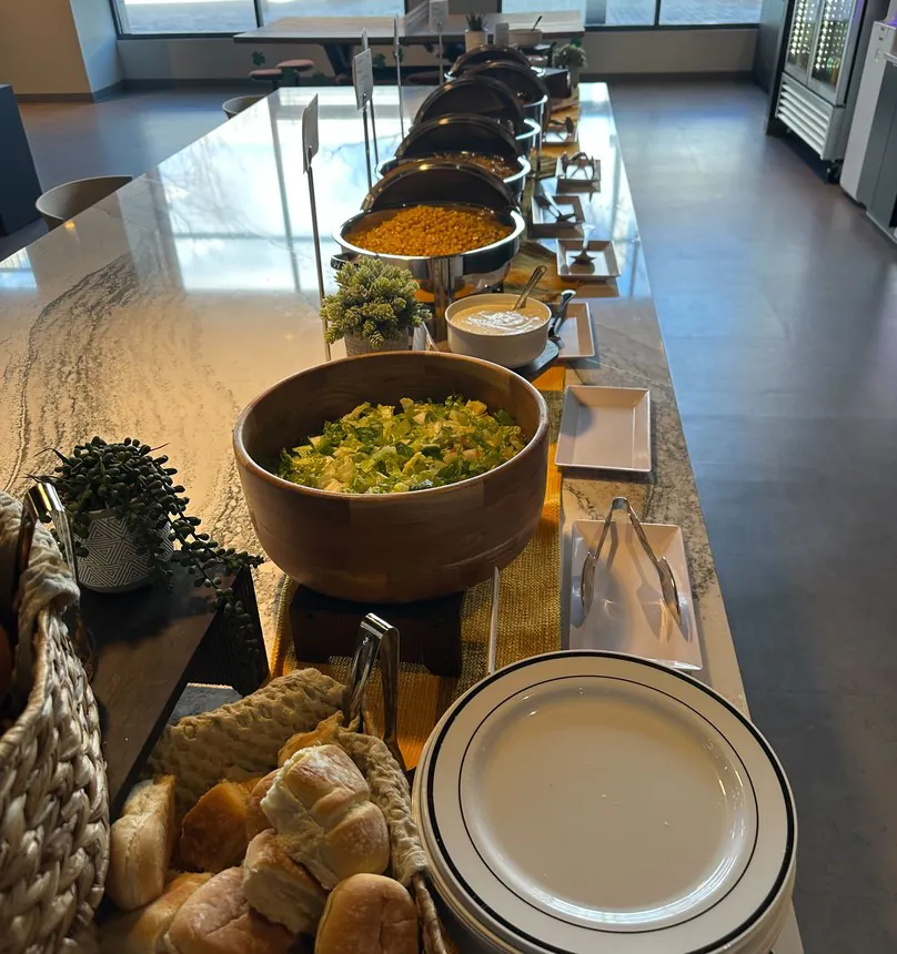 Affordable Hero Office lunch buffet with a salad bowl, dinner rolls and chafing dishes
