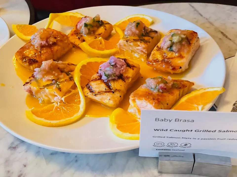 Baby Brasa grilled salmon at a client dinner Grilled salmon filets in a passion fruit reduction with orange slices on a white platter, with a Baby Brasa label card