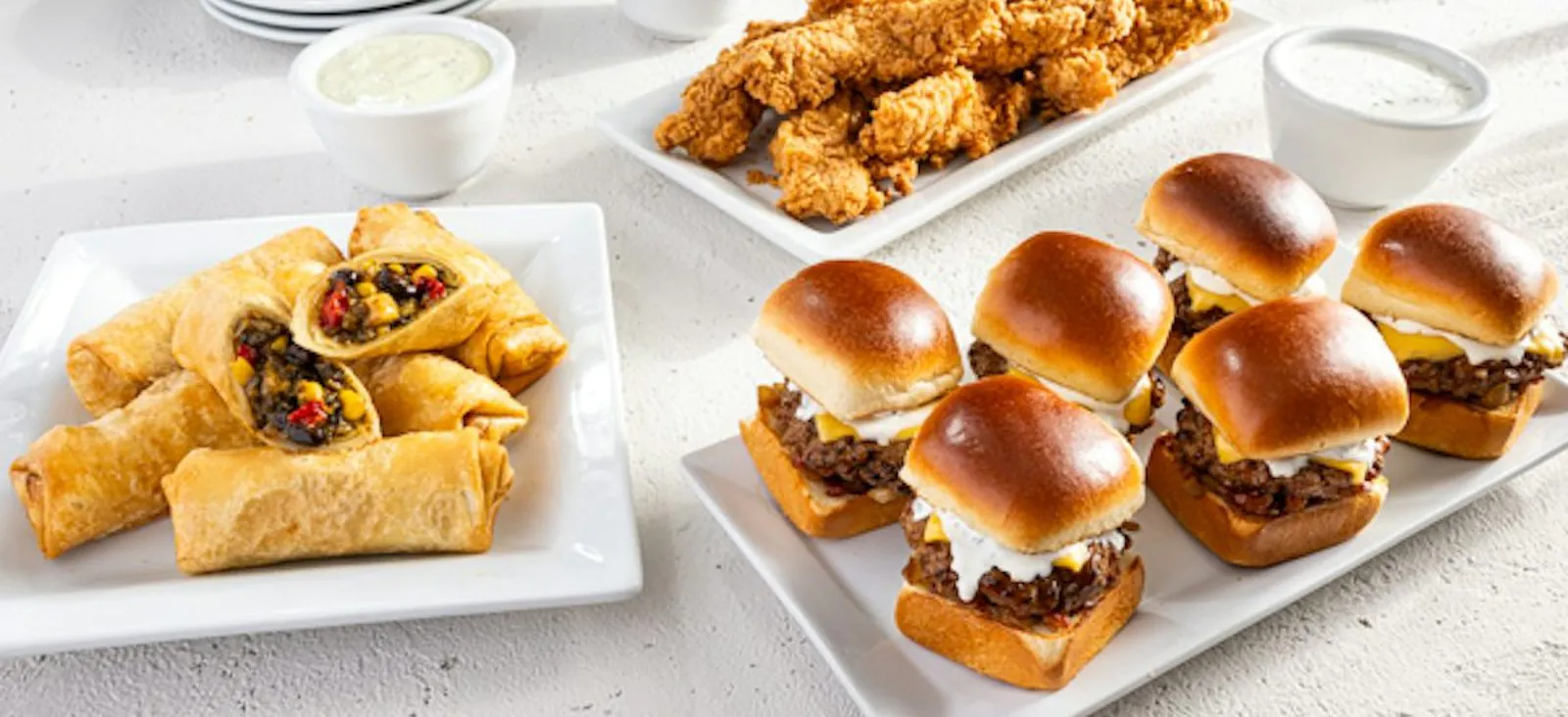 Chili's party platters on a light stone table: Southwestern Eggrolls cut open to show black beans and corn, a plate of Chicken Crispers, a platter of Big Mouth Bites sliders and bowls of ranch