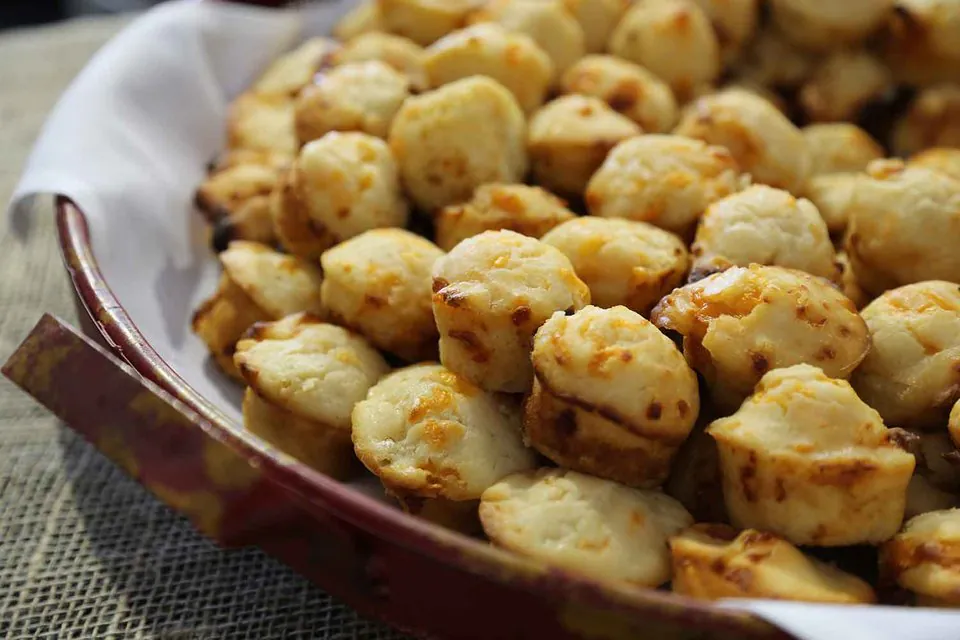 A red enamel dish piled with Jim 'N Nick's cheese biscuits, golden and studded with cheddar, on a white napkin over burlap