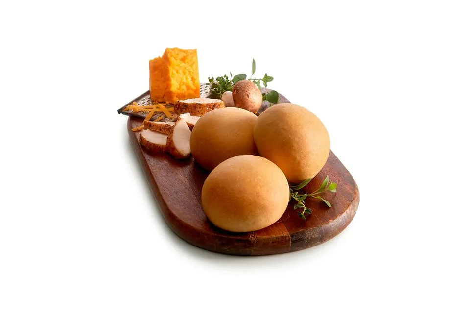 Three round Italian chicken kolaches on a dark wooden board beside sliced roast chicken, a block of cheddar, shredded cheese, mushrooms and fresh herbs