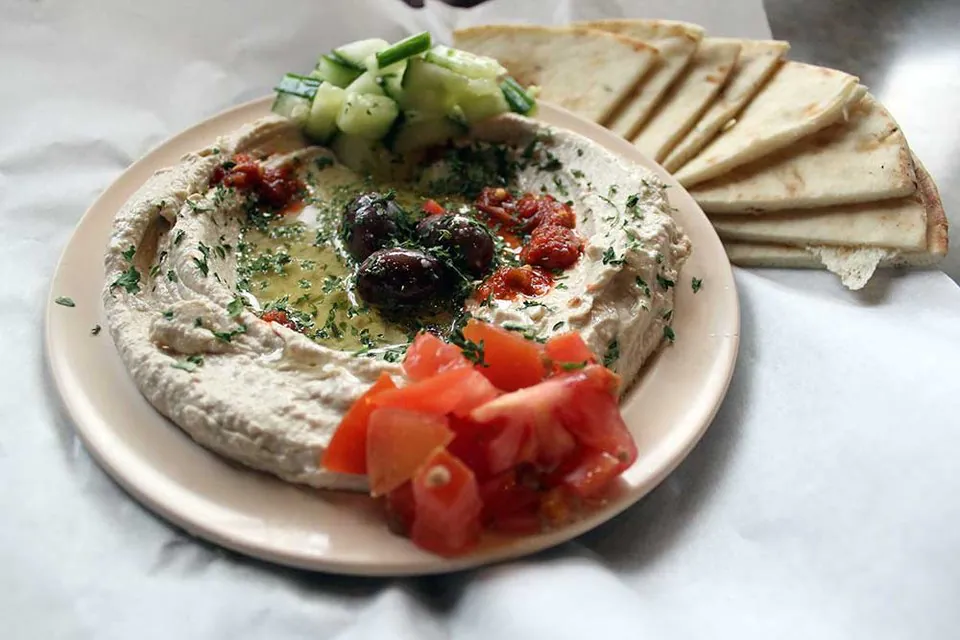 Hummus with pita from Mr. Gyros A plate of hummus topped with olive oil, kalamata olives, chopped tomato and cucumber, with triangles of warm pita