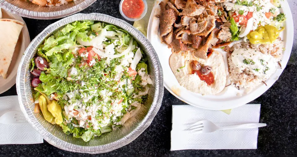A Mr. Gyros gyro plate and Greek salad A gyro plate with sliced lamb and beef, rice, hummus and tzatziki beside a foil tray of Greek salad with feta, olives and pepperoncini