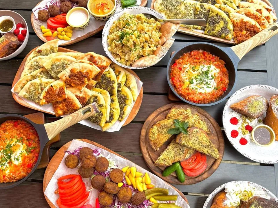 A Mr. Gyros spread with falafel, za'atar flatbreads and shakshuka An overhead spread of Mediterranean dishes on a wooden table: falafel with pickles and tomato, za'atar flatbreads, shakshuka in a skillet, an egg scramble with pita and stuffed pastries