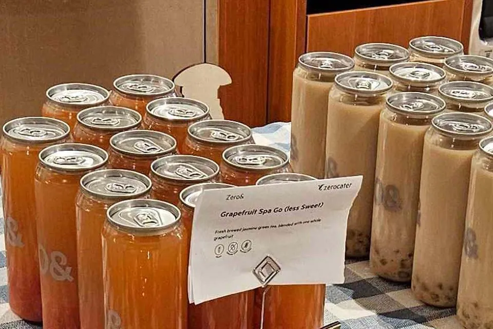 Rows of tall cans of grapefruit jasmine green tea and oolong milk tea on a checked tablecloth, with an ingredient card in front