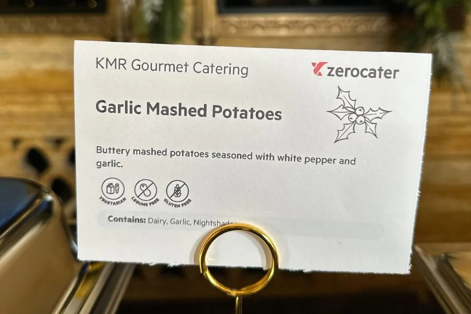 Printed dish card for garlic mashed potatoes on a gold stand, with a short description, vegetarian, legume-free and gluten-free icons and a Contains line