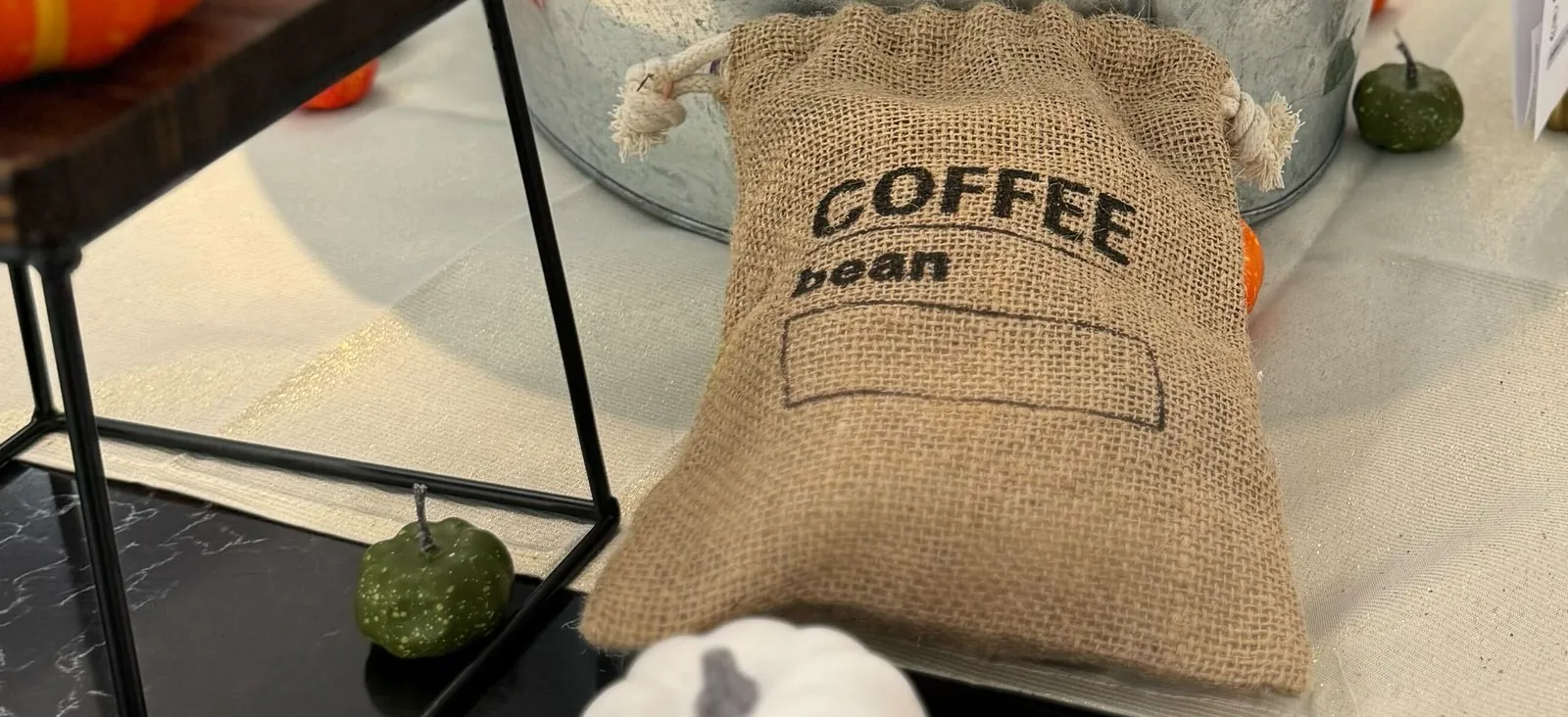 Burlap drawstring bag stenciled with the words coffee bean on an office counter, with small decorative gourds around it