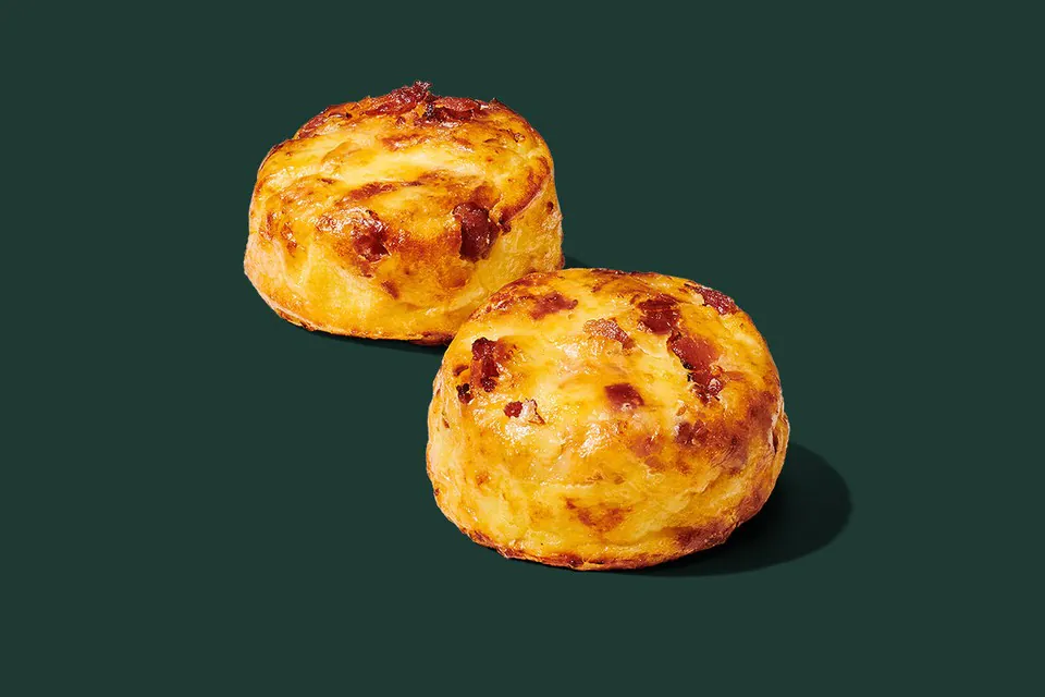 Two Starbucks Bacon and Gruyere Egg Bites, golden and studded with bacon, on a dark green background
