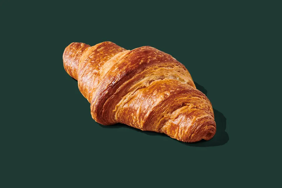 A single golden Starbucks Butter Croissant on a dark green background